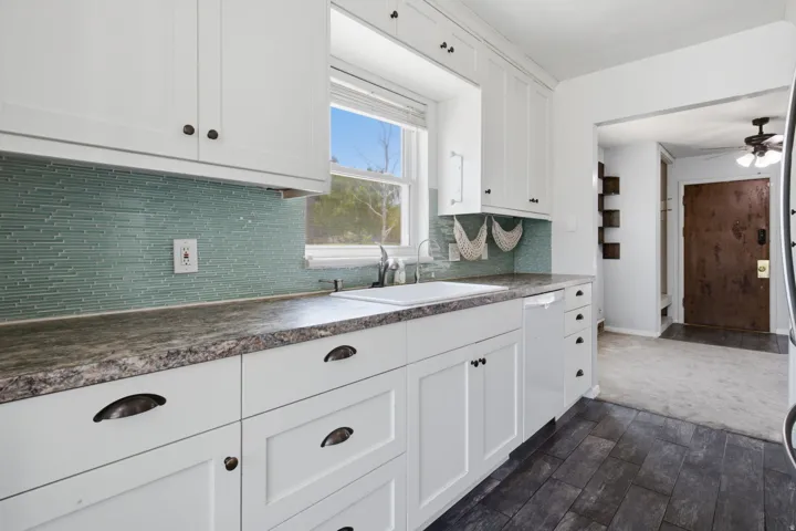 Bright kitchen featuring white cabinetry with oil-rubbed bronze hardware, granite countertops, and a turquoise subway tile backsplash