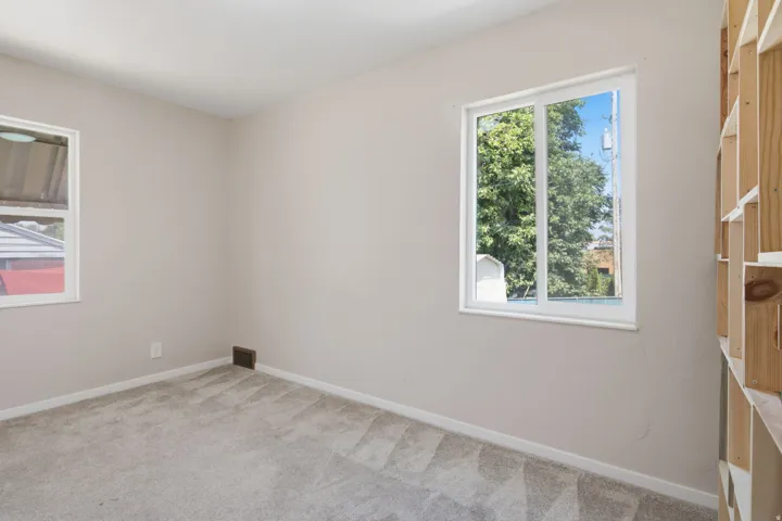 Bright, light-filled bedroom with dual windows framing natural outdoor scenery, neutral wall finishes, and carpeted flooring throughout