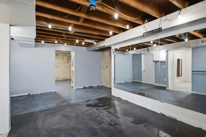 Exposed ceiling joists with string lighting, concrete flooring, and full-wall mirrors