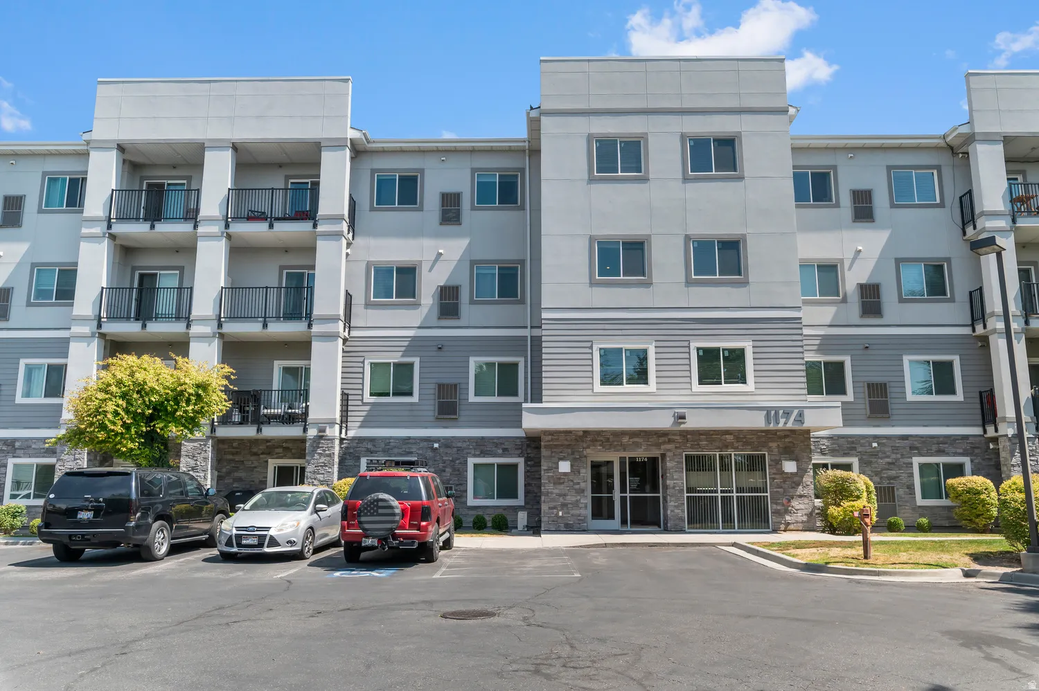 Multi-story building featuring a stone-clad base, balconies with metal railings, and a main entrance with glass doors