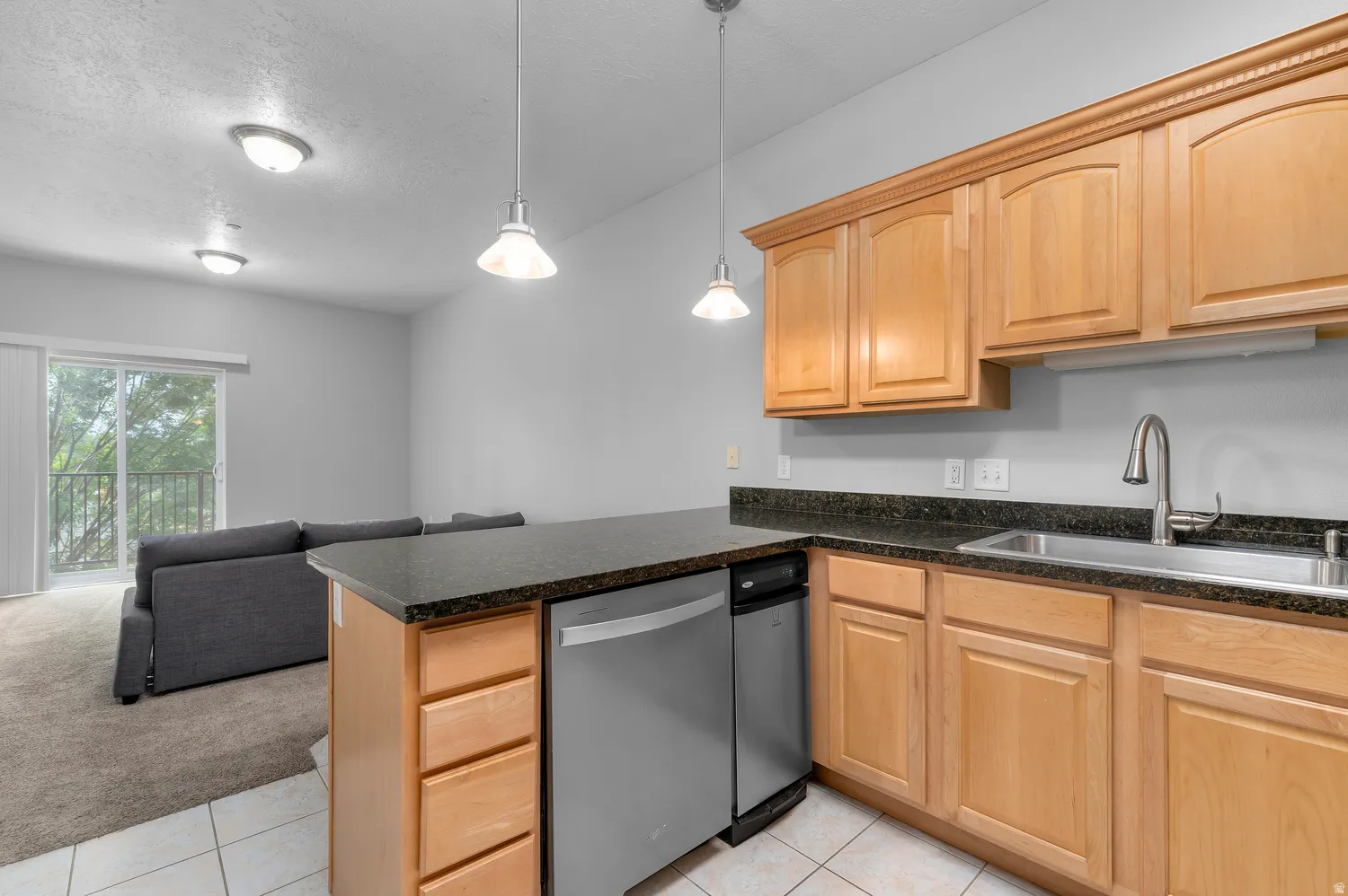 Kitchen featuring wood cabinetry, dark countertops, a stainless steel sink, and a built-in dishwasher