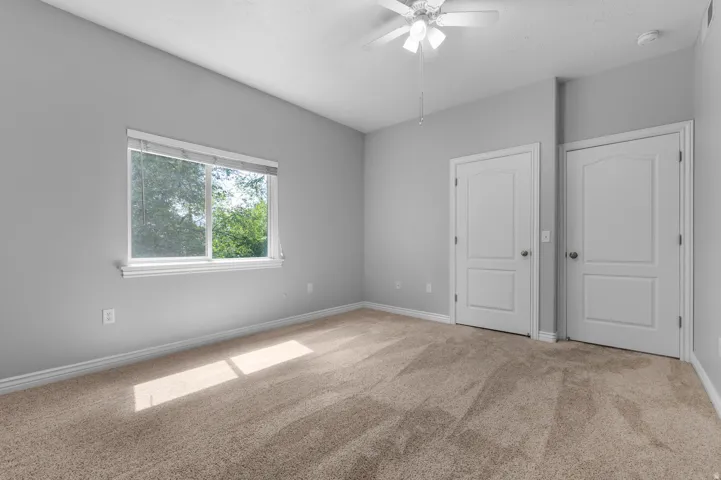 Light gray walls with a window, two white paneled doors, and a ceiling fan