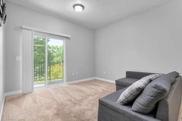Sliding glass door leading to a balcony with black metal railing, neutral carpet flooring, and white trim