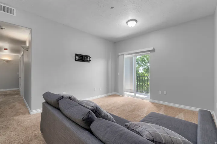 Carpeted flooring, light grey wall paint, white trim, sliding glass door, and a built-in balcony with a black metal railing