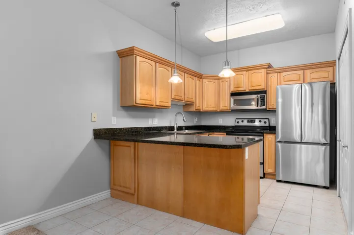 Kitchen featuring wood cabinetry, dark countertops, tile flooring, stainless steel appliances, and pendant lighting