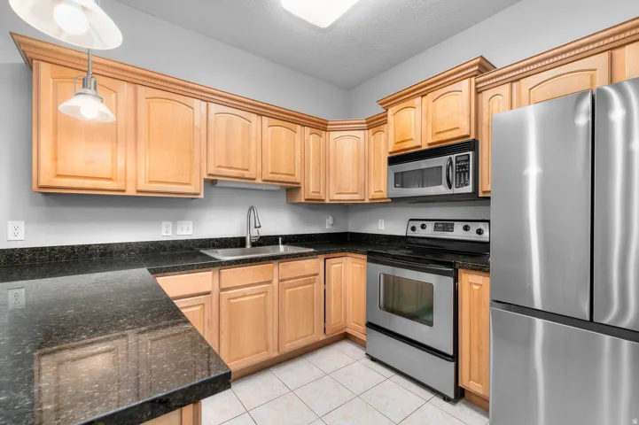 Kitchen featuring stainless steel appliances, wood cabinetry, dark countertops, and tiled flooring