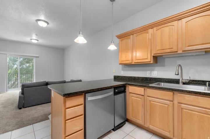 Kitchen featuring wood cabinetry, dark countertops, a stainless steel sink, and a built-in dishwasher