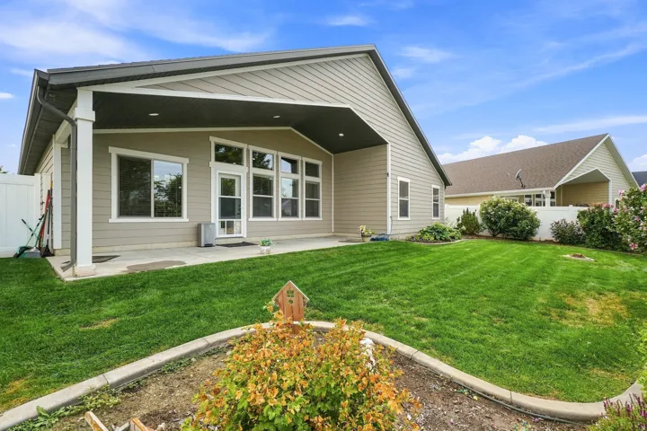 Expansive backyard featuring a covered patio, manicured lawn, garden bed, and white privacy fencing