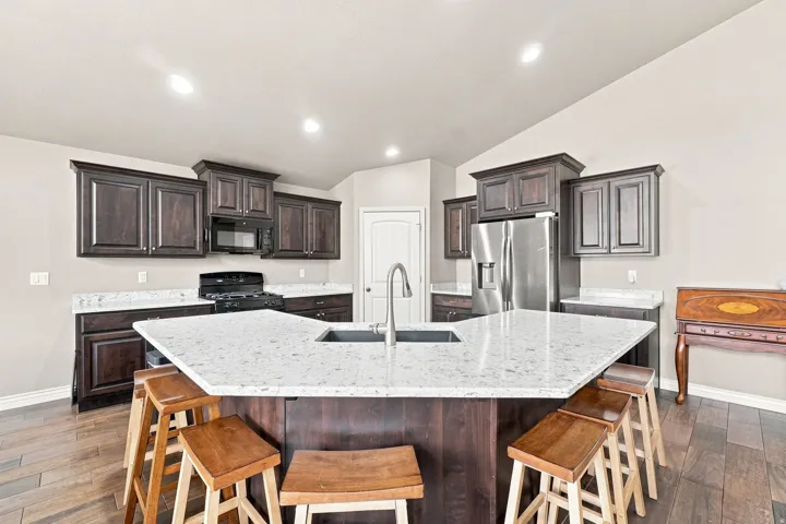 Kitchen featuring dark wood cabinetry, light-colored countertops, stainless steel refrigerator, built-in microwave, and wood-finish flooring