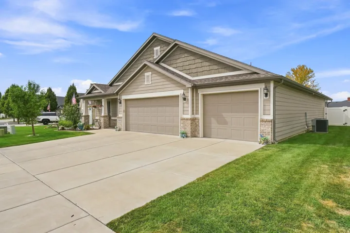Two-car garage with overhead doors, an additional one-car garage, concrete driveway, and a covered front entry with stone columns