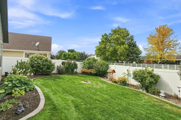 Expansive backyard featuring a professionally manicured lawn, curved planting beds with mature landscaping, white vinyl fencing, and established shade trees