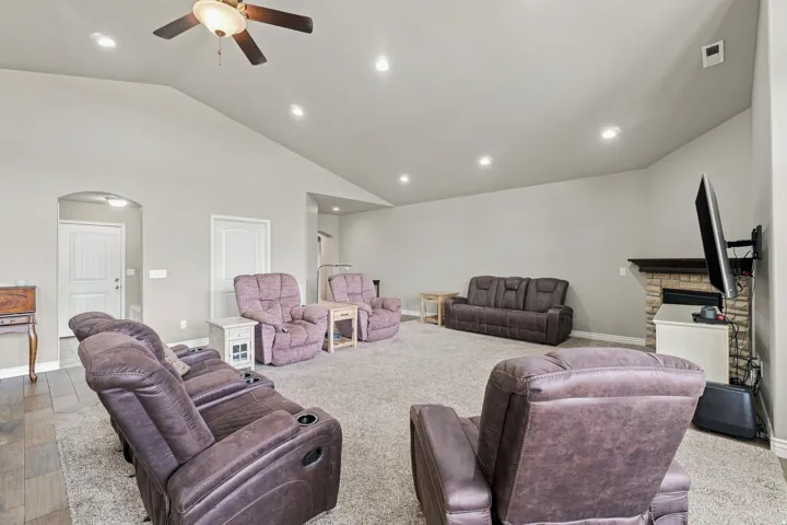 Vaulted ceiling with a ceiling fan, recessed lighting, stone fireplace, carpeted flooring, and wood-finish flooring