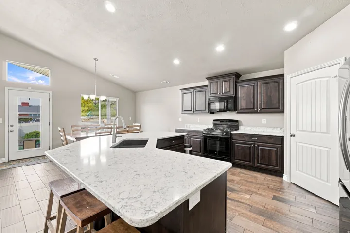 Vaulted ceiling kitchen featuring an expansive island with an undermount sink, dark wood-finish cabinetry, stainless steel appliances, and a tiled dining area