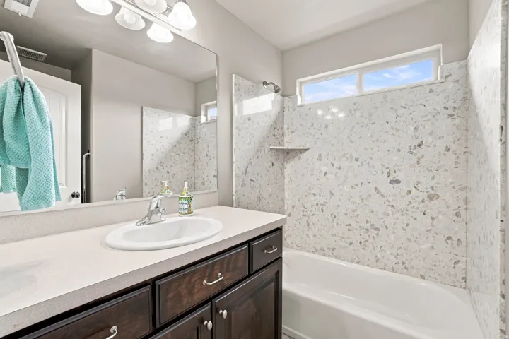Built-in bathtub with tiled surround featuring an integrated shelf, a single vanity with an integrated sink, a large wall-mounted mirror, and an overhead window