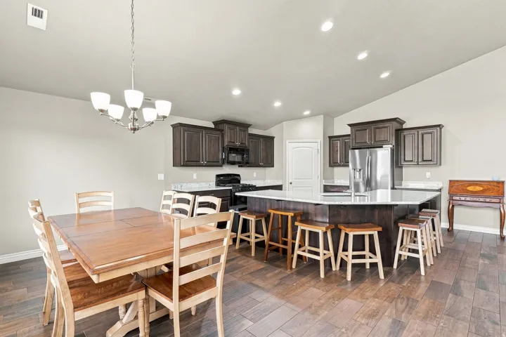Wood-finish flooring throughout, vaulted ceiling with recessed lighting, dark wood cabinetry, light-toned countertops, and a kitchen island with seating
