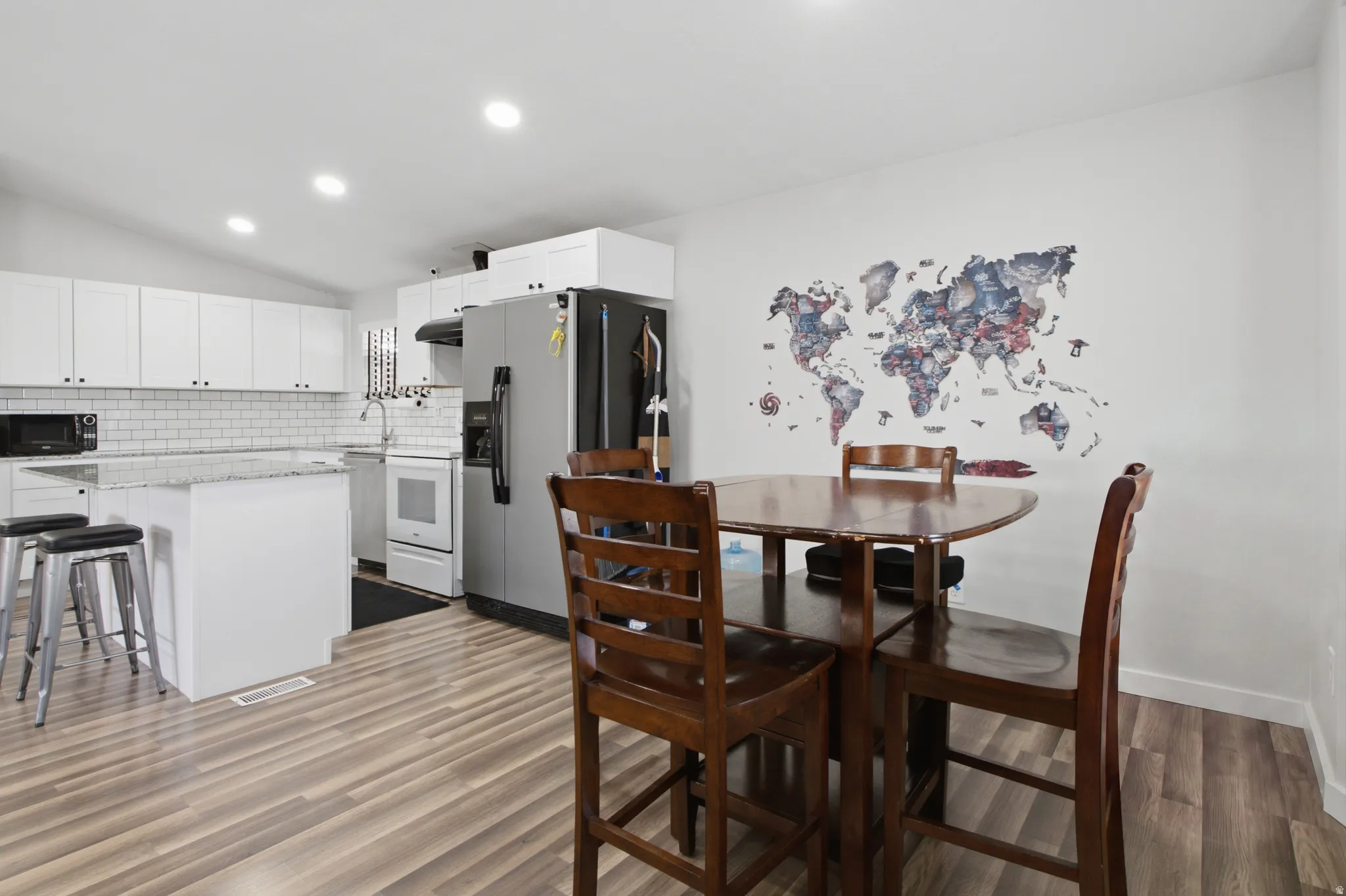 Wood-finish flooring, white cabinetry, subway tile backsplash, stainless steel appliances, and a breakfast bar