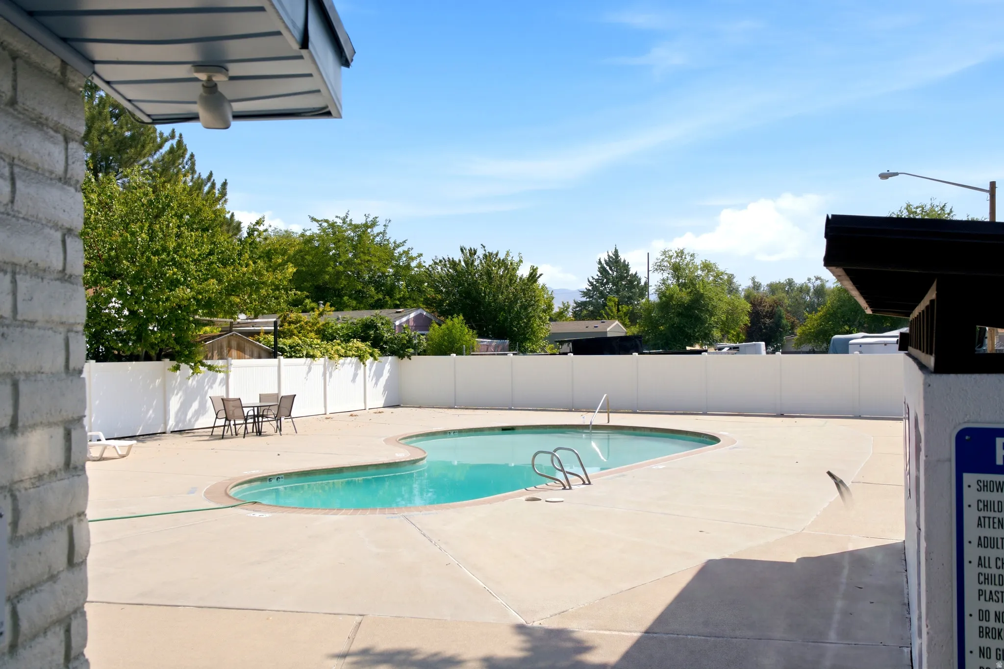 Curved swimming pool with integrated steps, surrounded by a concrete pool deck and white privacy fencing