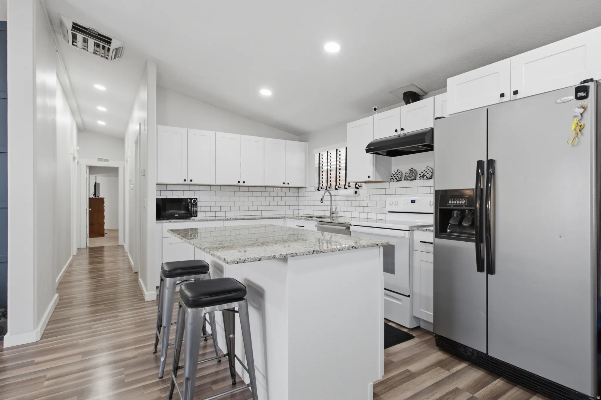 Kitchen featuring white shaker cabinetry, granite countertops, subway tile backsplash, and wood-finish flooring