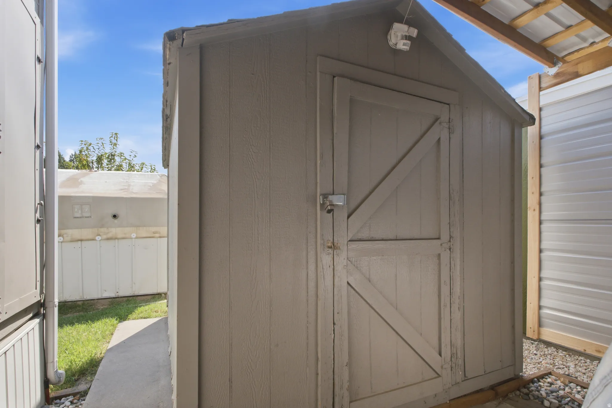 Wood-sided shed with a gable roof, featuring a wood door with diagonal bracing and metal hardware