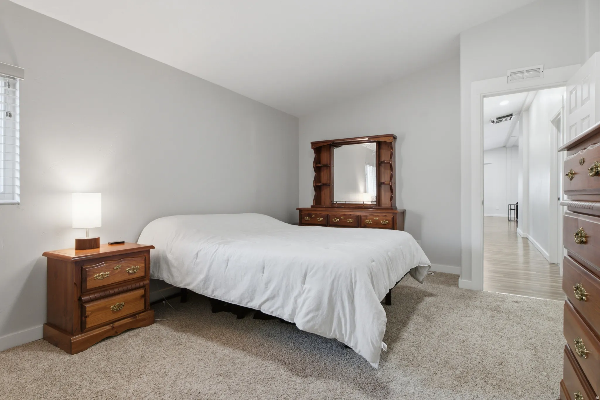 Light gray wall paint, textured carpeting, white trim, window with blinds, and an entryway with wood-finish flooring