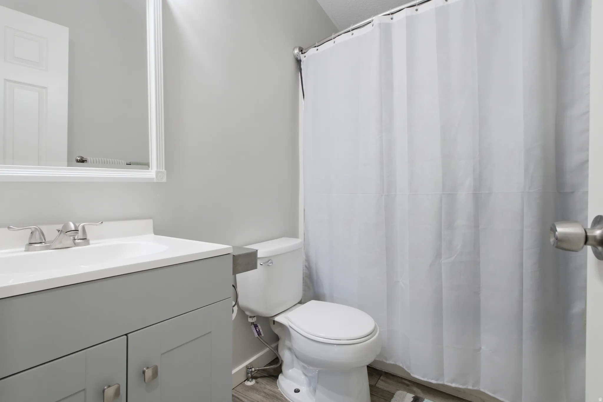 Vanity with integrated sink, brushed nickel faucet, framed mirror, toilet, and shower with curtain rod