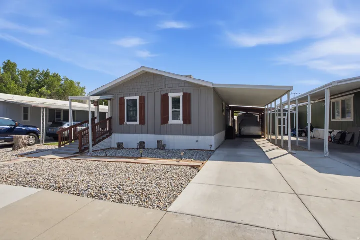 Manufactured home with gray siding, contrasting brown shutters, an attached carport, and a concrete driveway