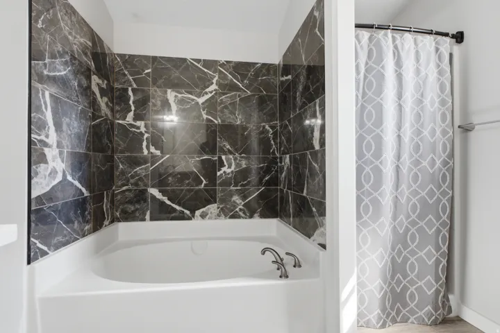 Built-in soaking tub with a deck-mounted faucet and dark marble-look tile surround