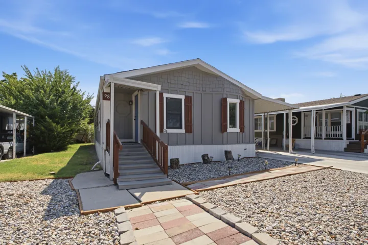 Grey exterior siding with decorative wood shutters, covered entry, and a paved walkway