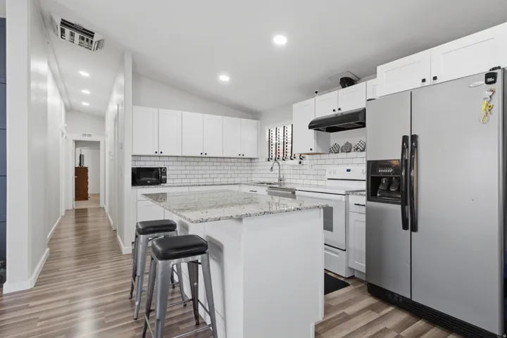 Kitchen featuring white shaker cabinetry, granite countertops, subway tile backsplash, and wood-finish flooring
