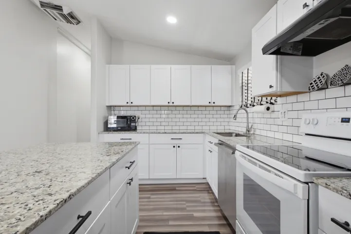 White shaker cabinetry with black hardware, granite countertops, subway tile backsplash, stainless steel sink, and wood-finish flooring