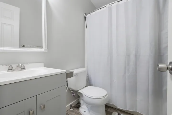 Vanity with integrated sink, brushed nickel faucet, framed mirror, toilet, and shower with curtain rod
