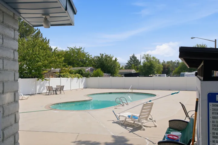 Swimming pool with concrete surround, white privacy fencing, and surrounding trees