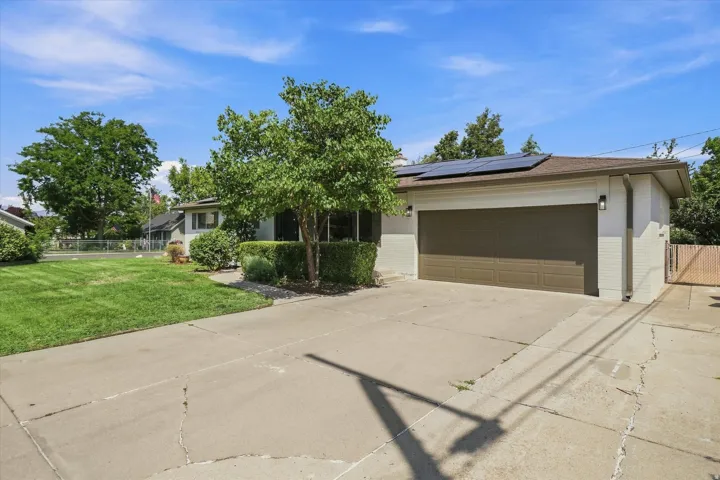 Front exterior featuring a two-car garage, concrete driveway, solar panels, and mature landscaping