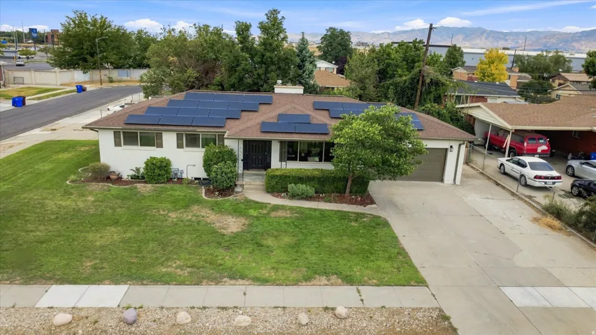 Ranch-style residence featuring a brown shingle roof, solar panel array, attached garage, and a concrete driveway