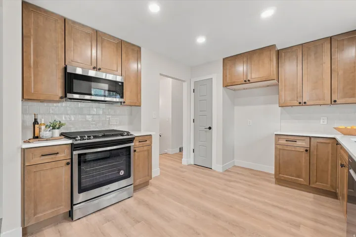 Kitchen featuring wood-finish cabinetry, stainless steel appliances, light-toned countertops, and a subway tile backsplash