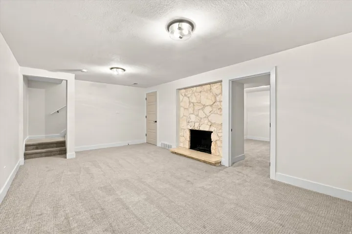 Stone-clad fireplace with a hearth, wall-to-wall carpeting, and recessed lighting