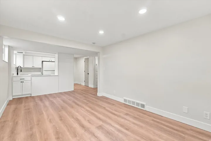 ADU Spacious living area with wood-finish flooring, recessed lighting, and a modern kitchen featuring white cabinetry, a black gooseneck faucet, and a built-in refrigerator