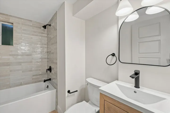 Bathroom featuring a tub/shower combination with subway tile surround, matte black fixtures, a wood-finish vanity, and a rectangular sink