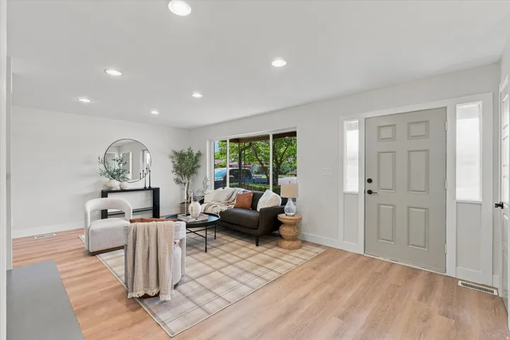 Recessed ceiling lighting, wood-finish flooring, light gray interior paint, light gray paneled entry door, and large window