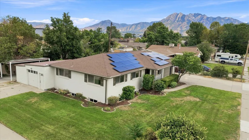 Residence featuring solar panels, a two-car garage, mature landscaping, and mountain scenery