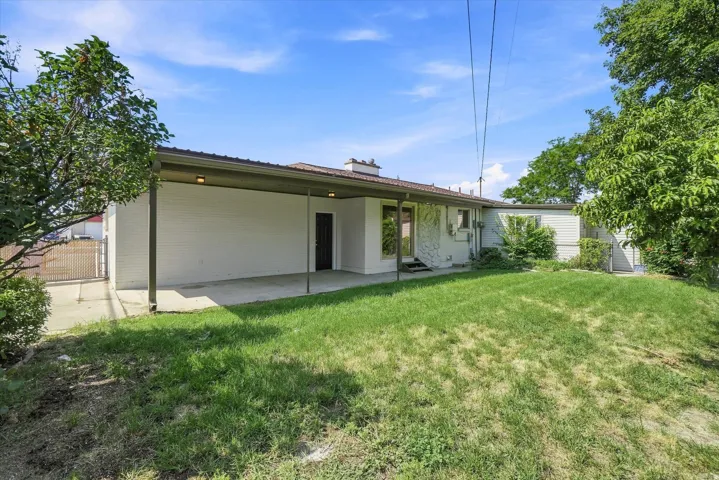 Expansive grassy yard with mature trees, a covered patio area, and a paved driveway