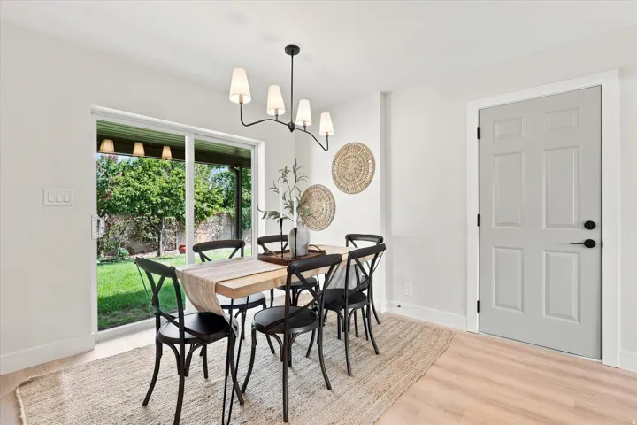 Sliding glass door leading to the backyard, light wood-finish flooring, contemporary chandelier, and a paneled interior door with matte black hardware