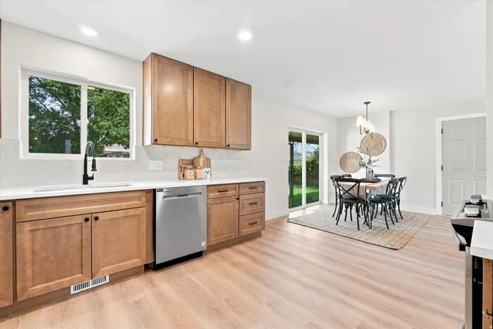 Kitchen with wood-finish cabinetry, stainless steel dishwasher, white subway tile backsplash, and light-toned flooring
