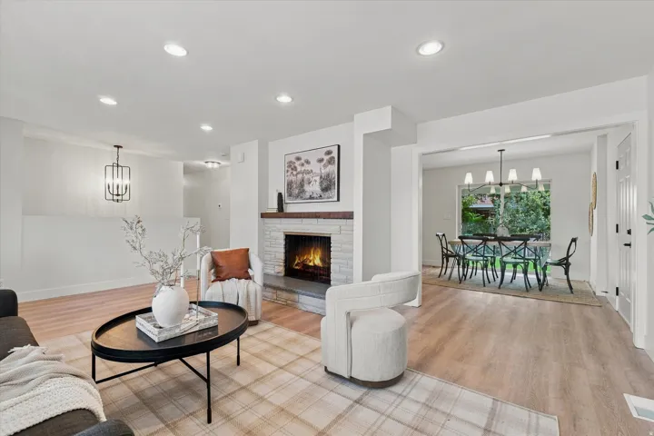 Stone-front fireplace with a wood mantel, recessed lighting, wood-finish flooring, and a dining area with a chandelier