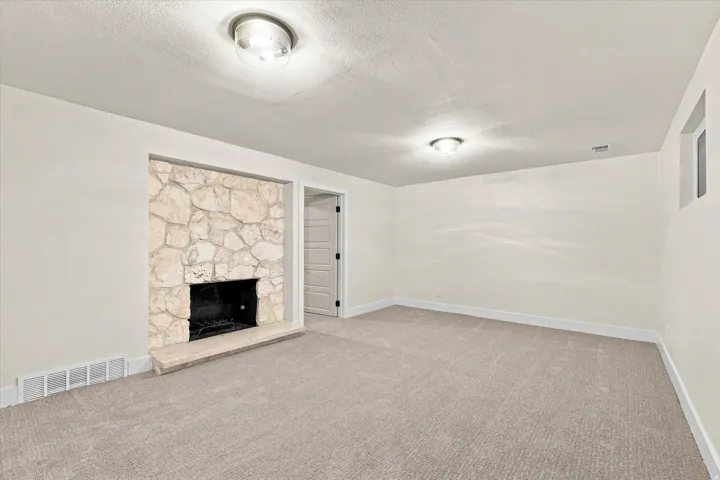 Neutral-toned carpeted flooring, stone-clad fireplace with hearth, and recessed entry