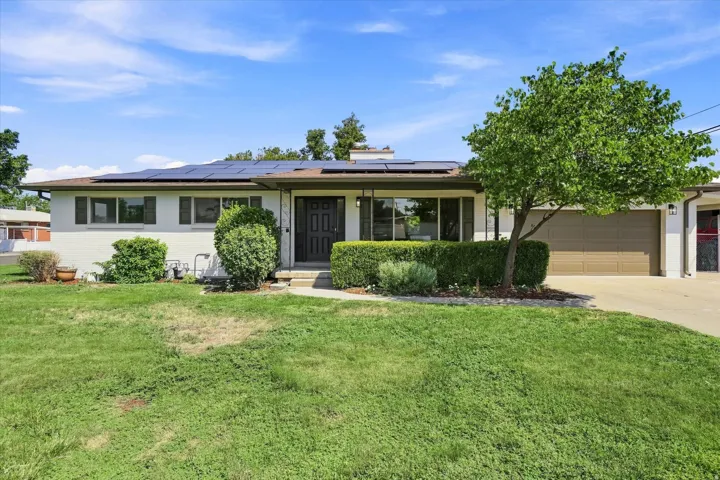 White exterior with dark shutters, front entry door, attached garage, and solar panels