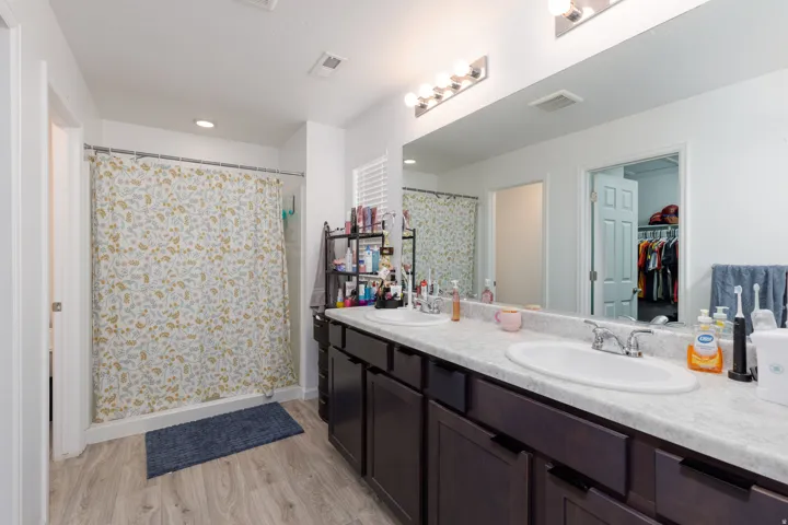 Spacious vanity with dual undermount sinks and extensive countertop space, wood-finish flooring, and a shower with a sliding glass door