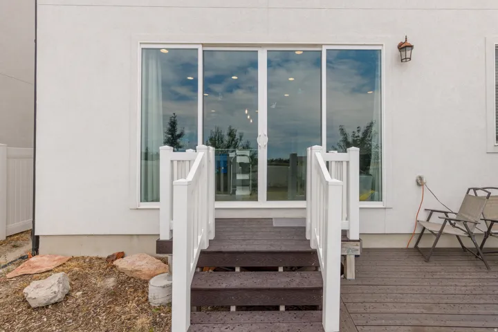 White stucco exterior featuring a sliding glass door, outdoor wall sconce, and a multi-level deck with white railings