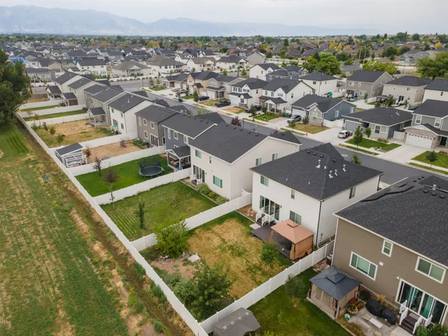 Residential neighborhood with a mountain backdrop, featuring a variety of home styles with dark shingle roofs and light-colored siding, and individual fenced backyards