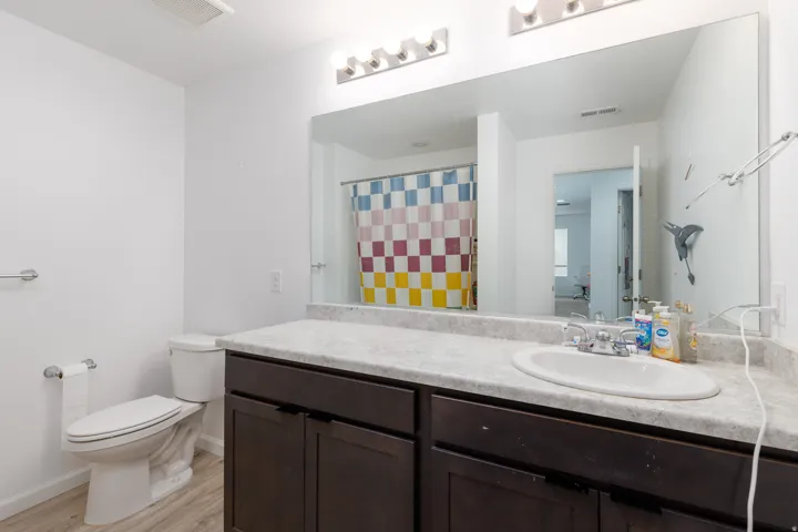 Modern bathroom featuring a dark wood vanity with an expansive quartz countertop, an undermount sink with chrome fixtures, and a large framed mirror with integrated lighting